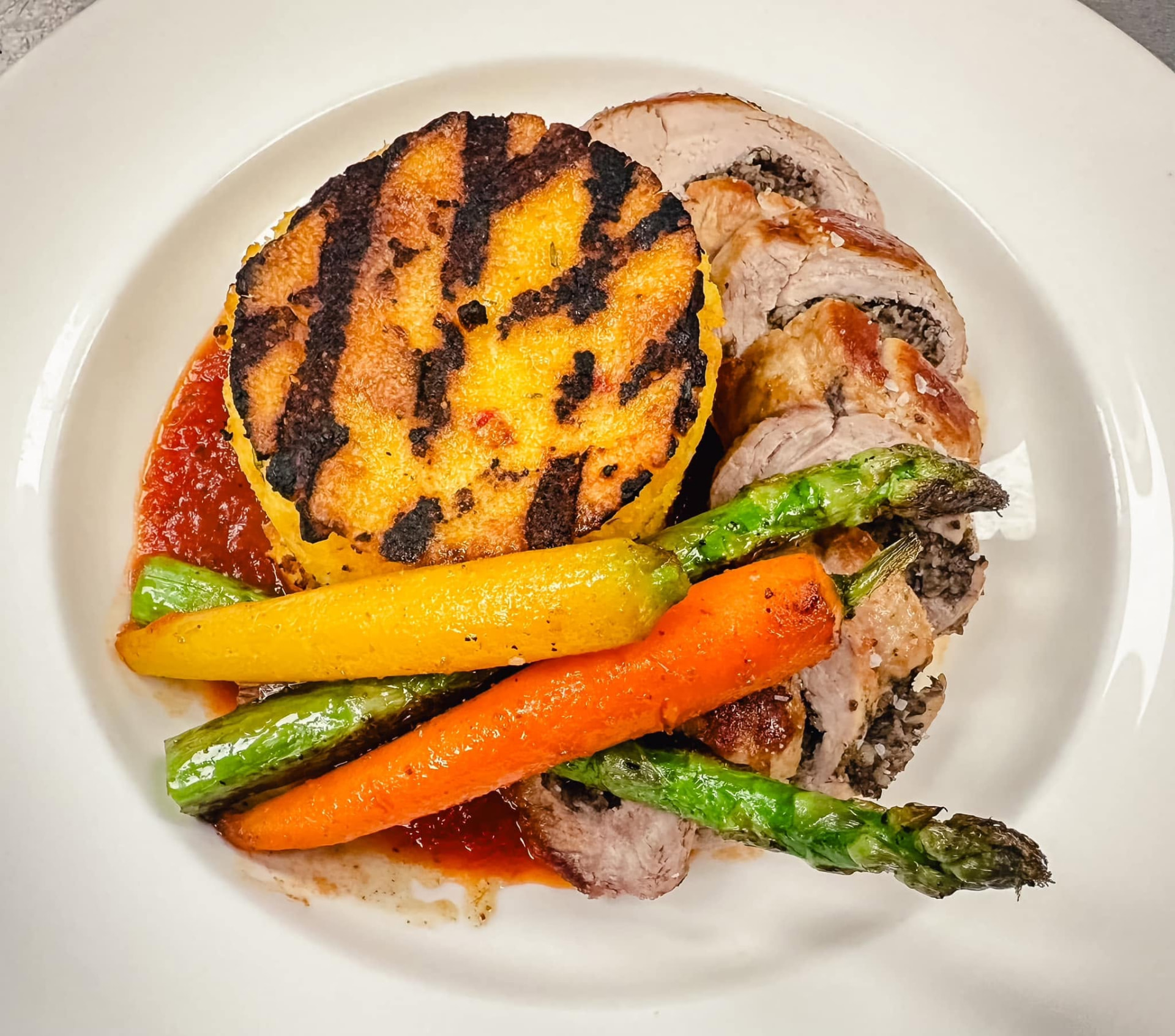 Sliced stuffed pork loin with grilled polenta cake, roasted carrots and asparagus