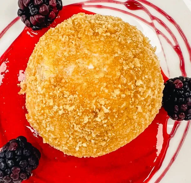 Crisp-coated dessert dome on bright berry coulis with blackberries