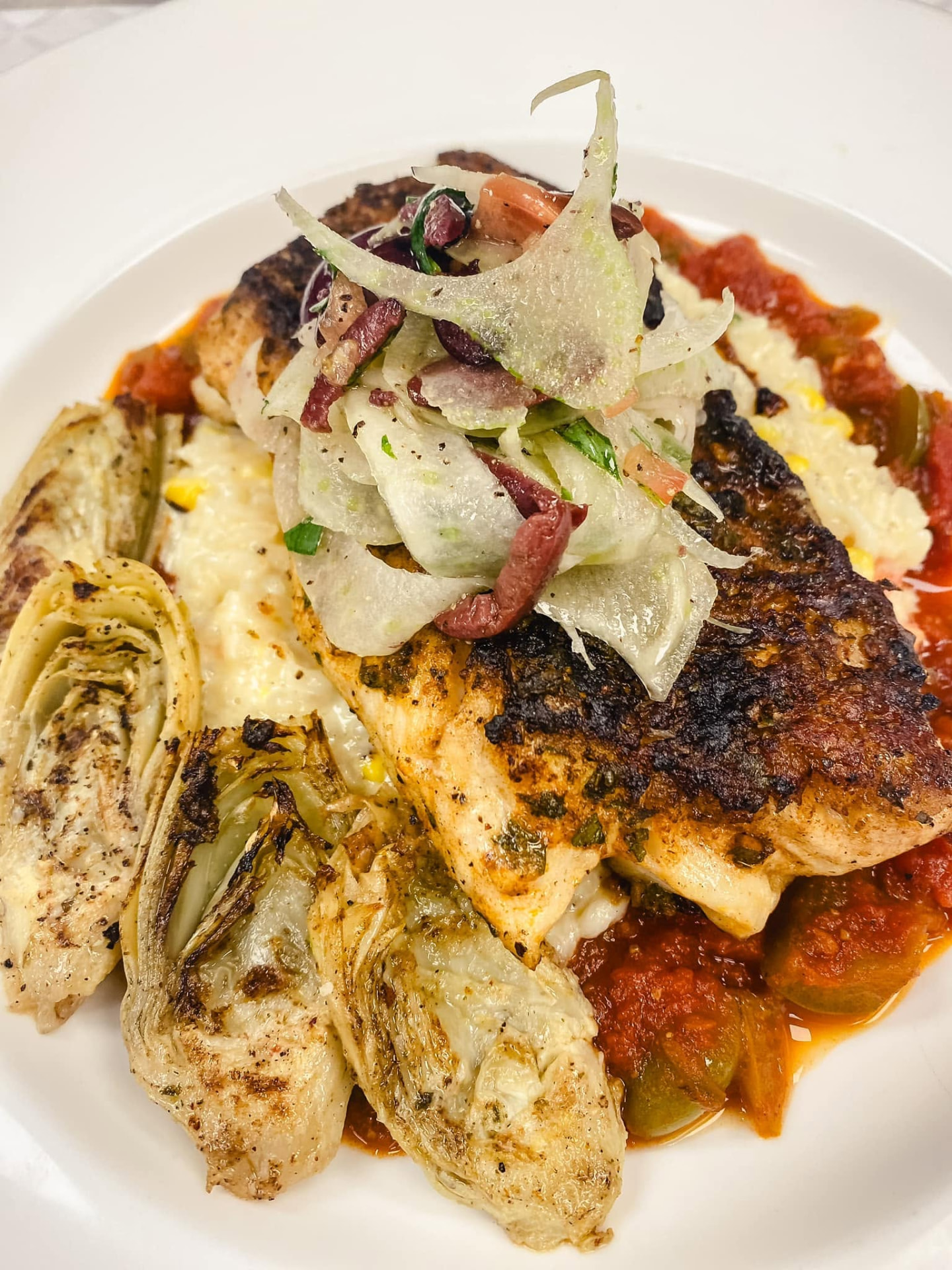 Blackened fish fillet with grilled artichoke hearts, tomato sauce and shaved fennel salad