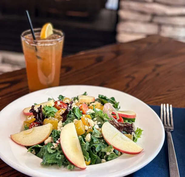 Kale salad topped with apple slices and golden beets beside an iced cocktail with an orange slice