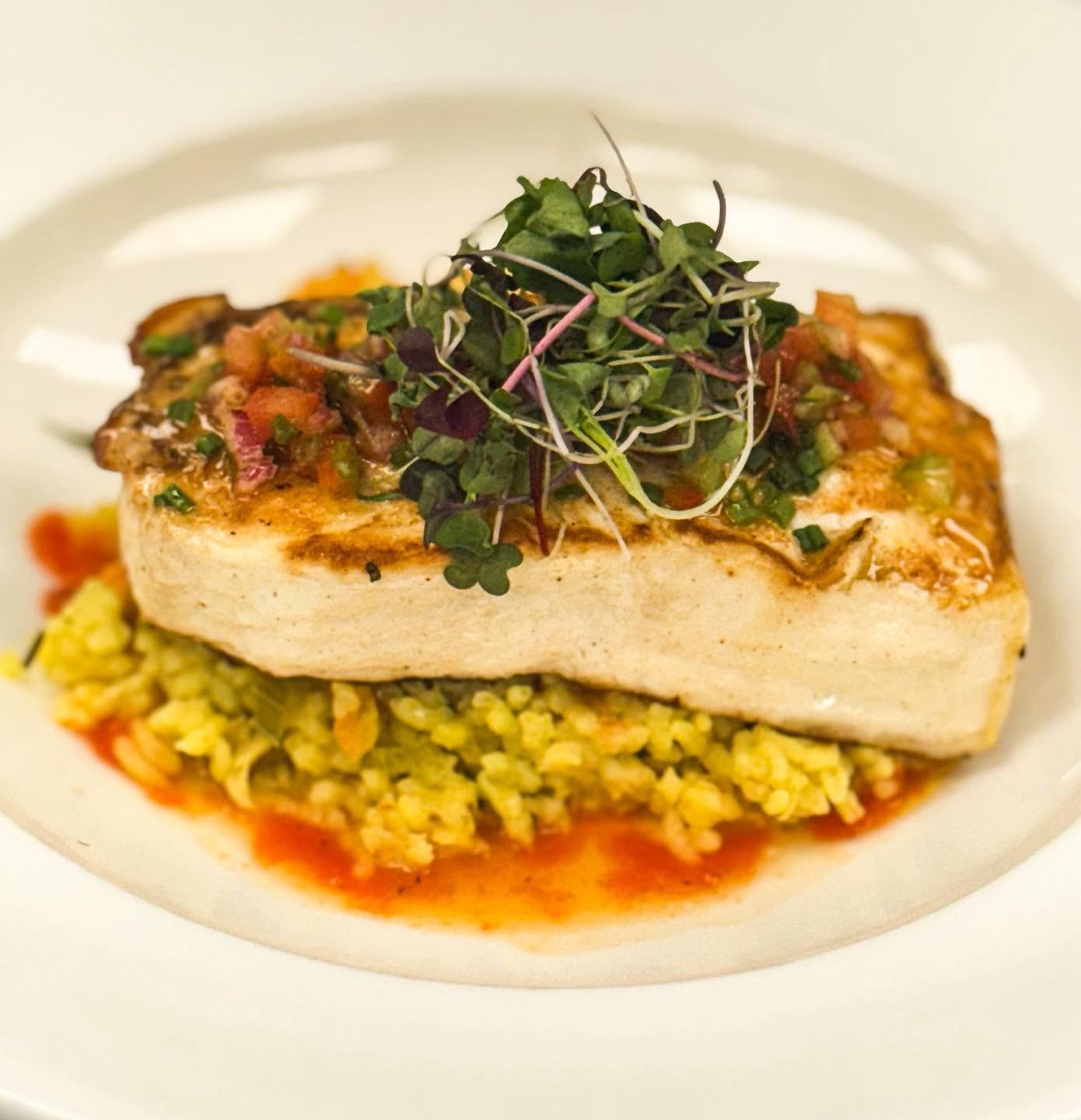 Seared white fish fillet over yellow rice with tomato salsa and microgreens