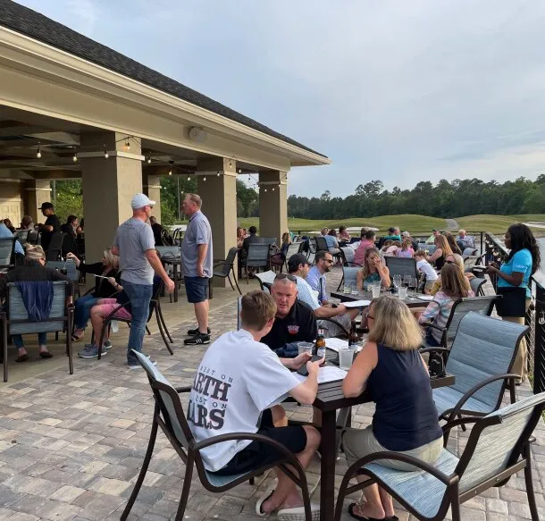 Guests gathered at tables on the covered patio overlooking the green golf course at dusk